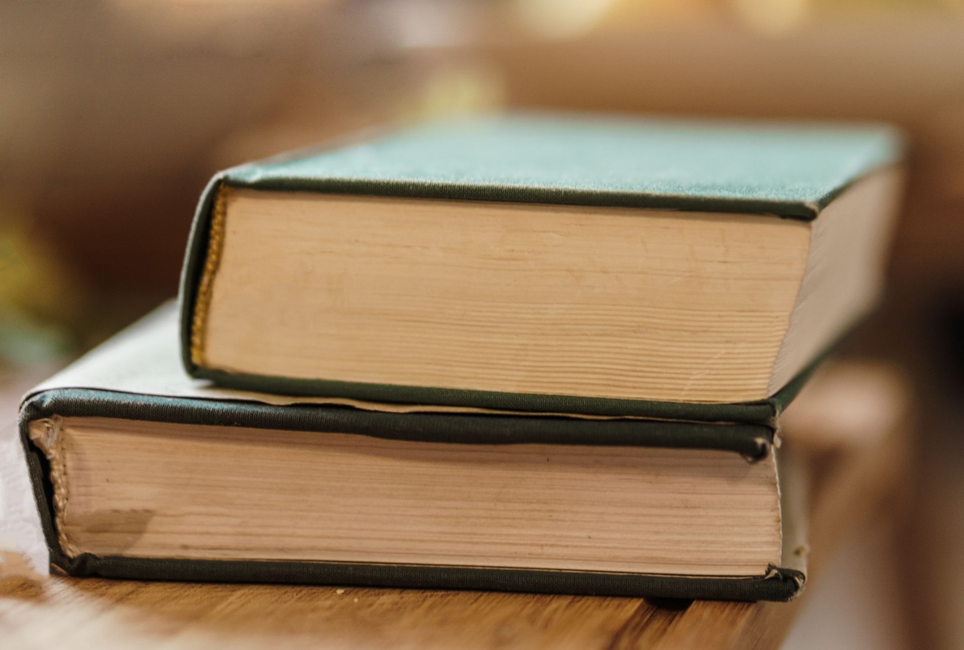 Close-up of vintage hardcover books stacked on a wooden table indoors.