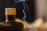Shiny bottle of alcohol with opaque glass and ribbed cap near fume in air on blurred background