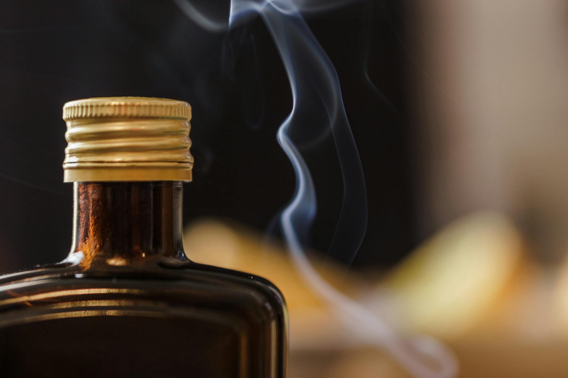 Shiny bottle of alcohol with opaque glass and ribbed cap near fume in air on blurred background