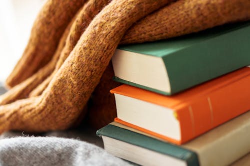 Shiny knitted textile on pile of big colorful textbooks with hard covers in sunlight