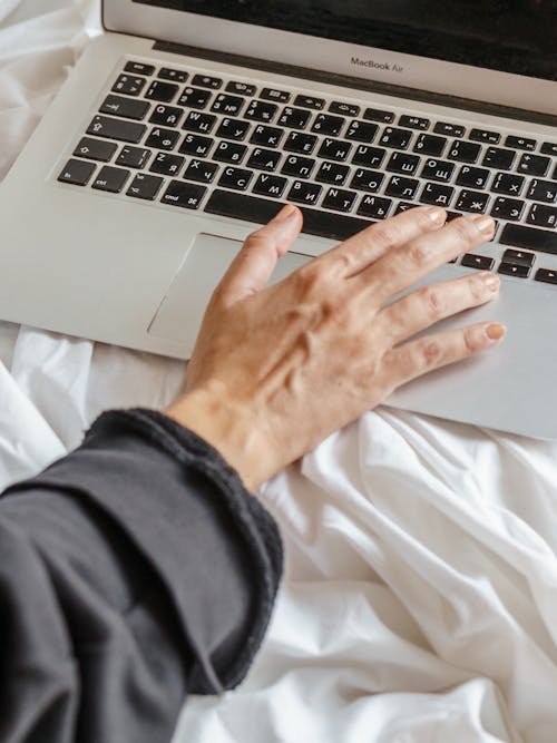 From above of crop anonymous female distance worker browsing internet on netbook on soft crumpled bed sheet at home