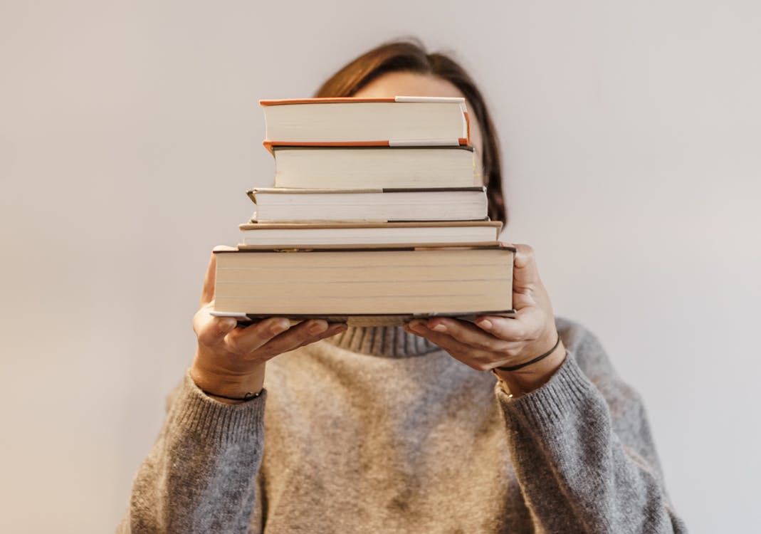 Free Person in Gray Sweater Carrying a Stack of Hardbound Books Stock Photo