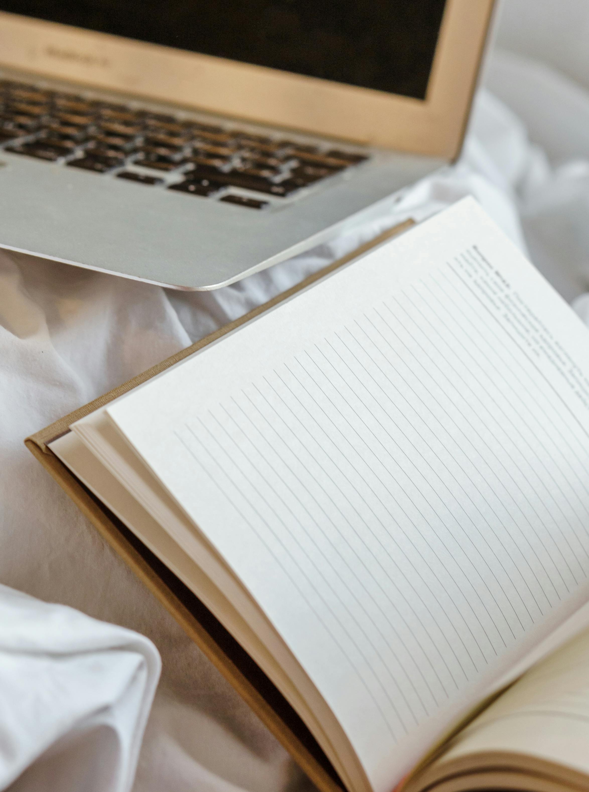 open diary near laptop on crumpled bed at home