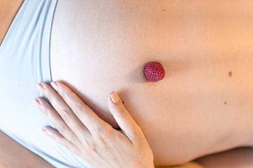Faceless pregnant woman caressing belly with fresh raspberry