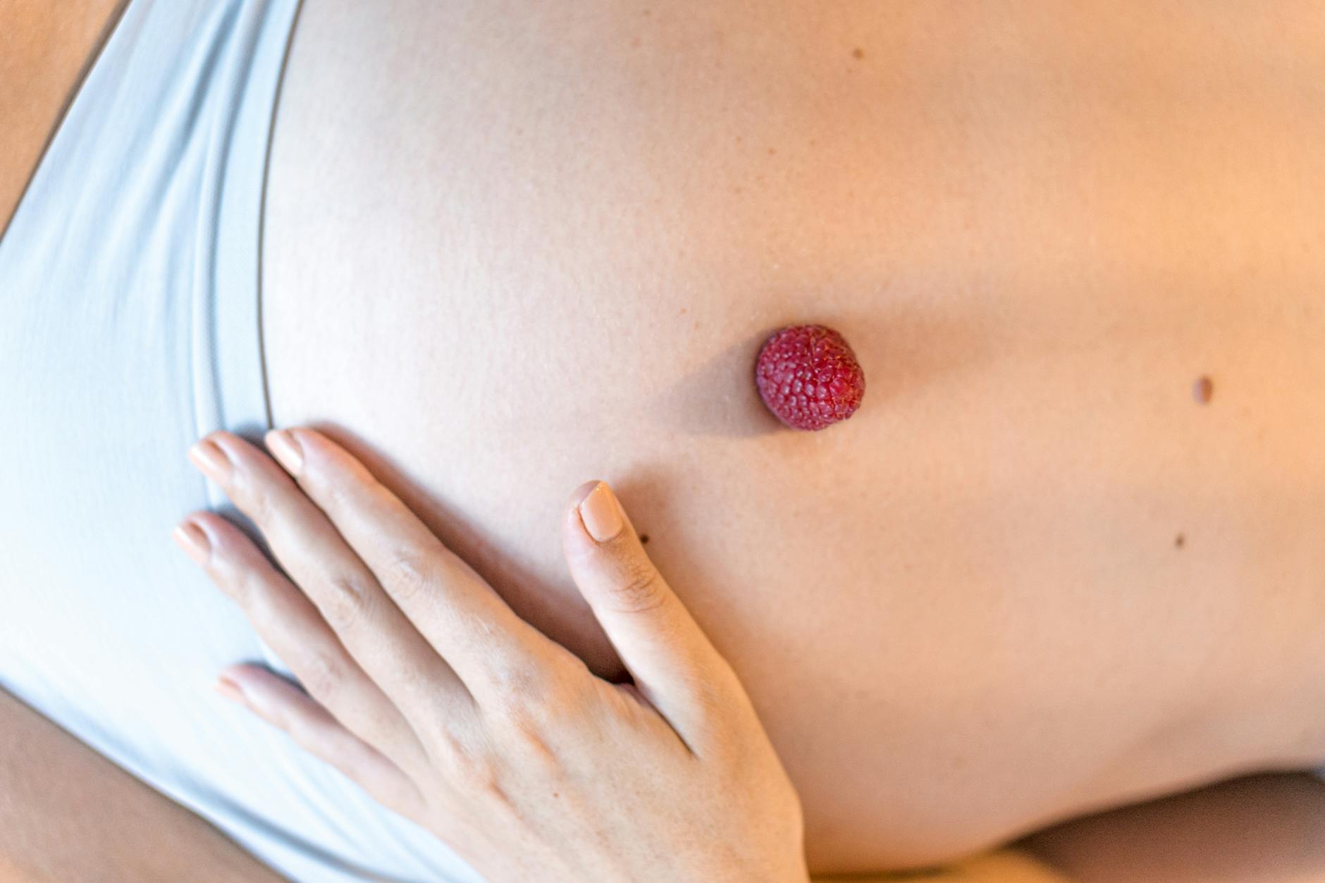 A close-up of a pregnant belly with a raspberry and hand, symbolizing maternal health and nature.