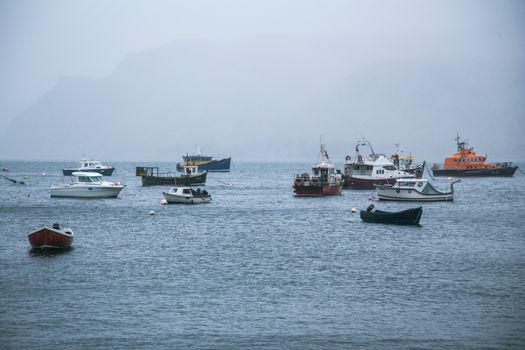 波光粼粼的蓝色河流上，漂浮着一艘钓鱼摩托艇，映衬着雾霭笼罩的阴沉山脉