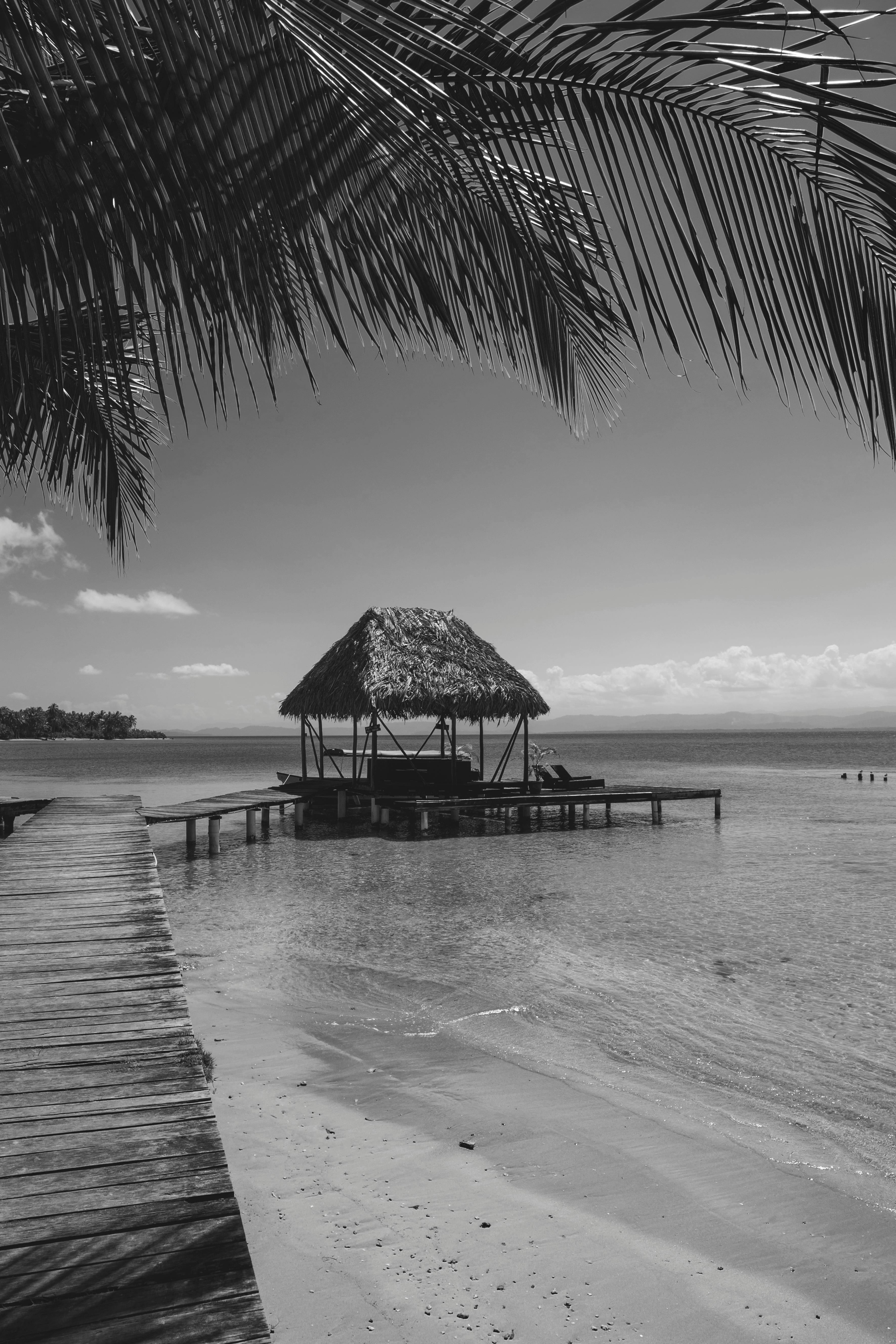 Black and white scenery of wooden bungalow on wharf near tranquil rippling sea on tropical island