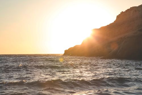 Free Scenic view of rippling waving sea near rough rocky cliffs against bright setting sun in early evening Stock Photo