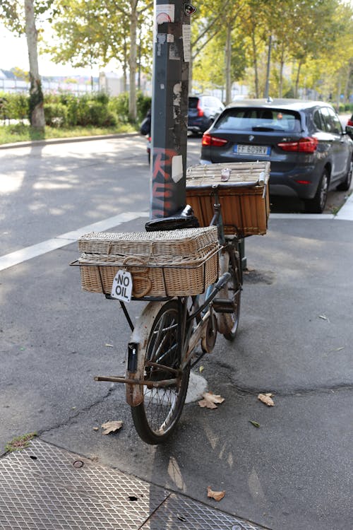 Free Old bicycle with wicker baskets parked near streetlight pole on sidewalk in sunny summer town Stock Photo