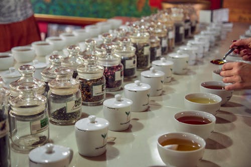 Crop anonymous female with teaspoon standing near table with assorted aromatic teas served for tea tasting session