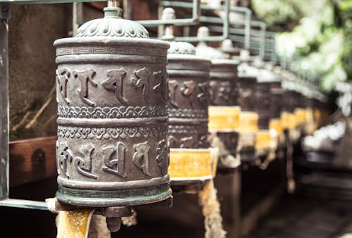 Row of oriental carved prayer wheels located in green Buddhist park on sunny weather