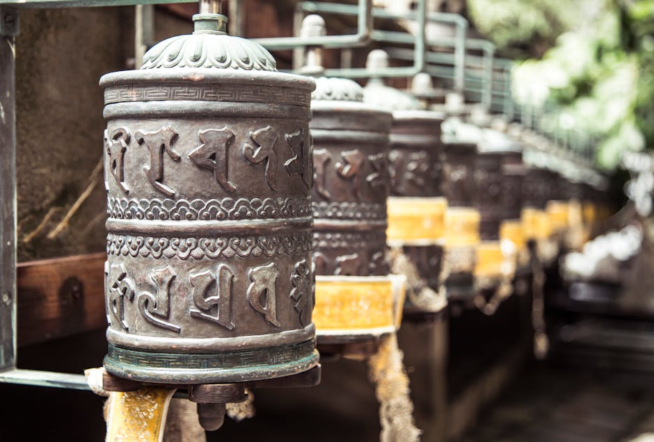 Row of oriental carved prayer wheels located in green Buddhist park on sunny weather