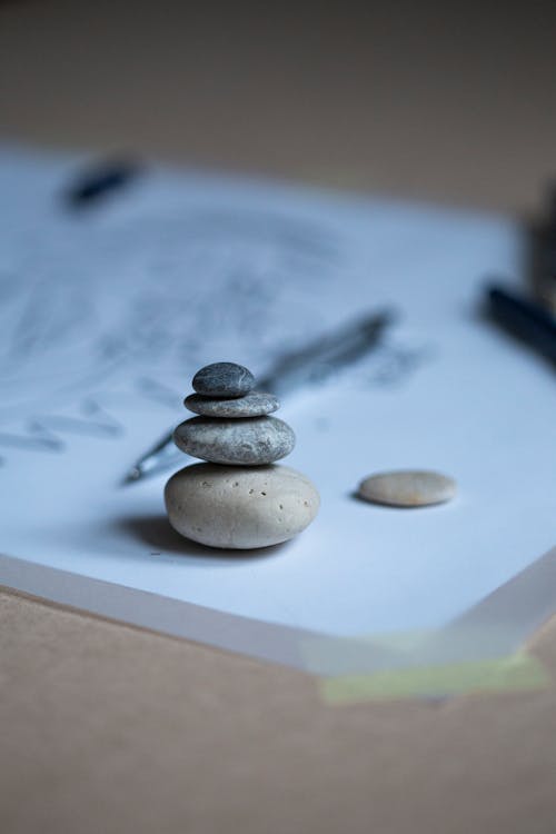 Composition of small stacked rock cairns placed on blurred white canvas near pen
