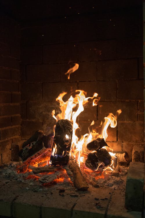 Bright burning firewood flaming in large brick fireplace in dark living room at night