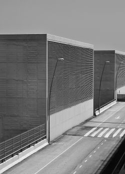 Black and white of concrete constructions with metal grid with fence located near asphalt road with marking lines on street in city