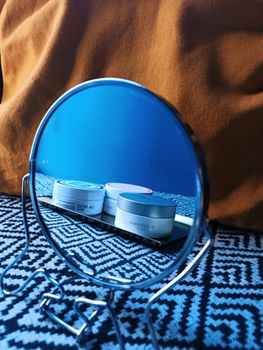 Aesthetic skincare products reflected in a stylish circular mirror on patterned tablecloth.