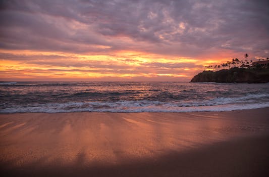 A tranquil sunset over a tropical beach with gentle waves and a vivid sky.