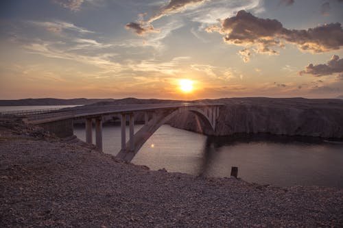 Free Picturesque view of old stone bridge over calm water in mountainous area under colorful sundown sky Stock Photo