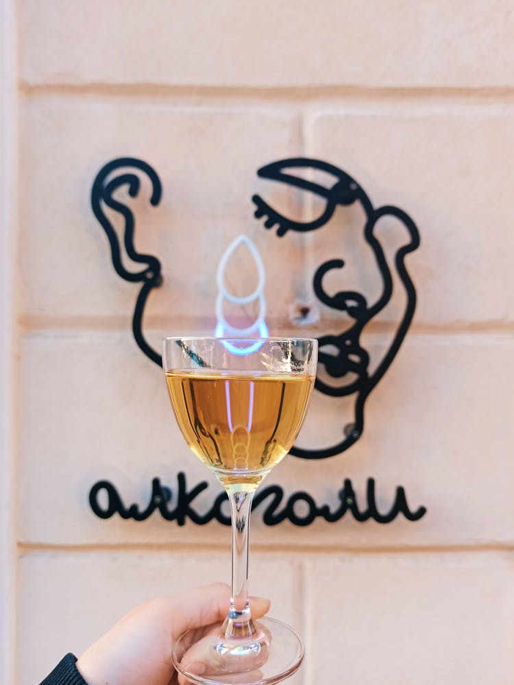 Woman Holding A Glass Of Champagne In Front Of A Companys Neon Logo 