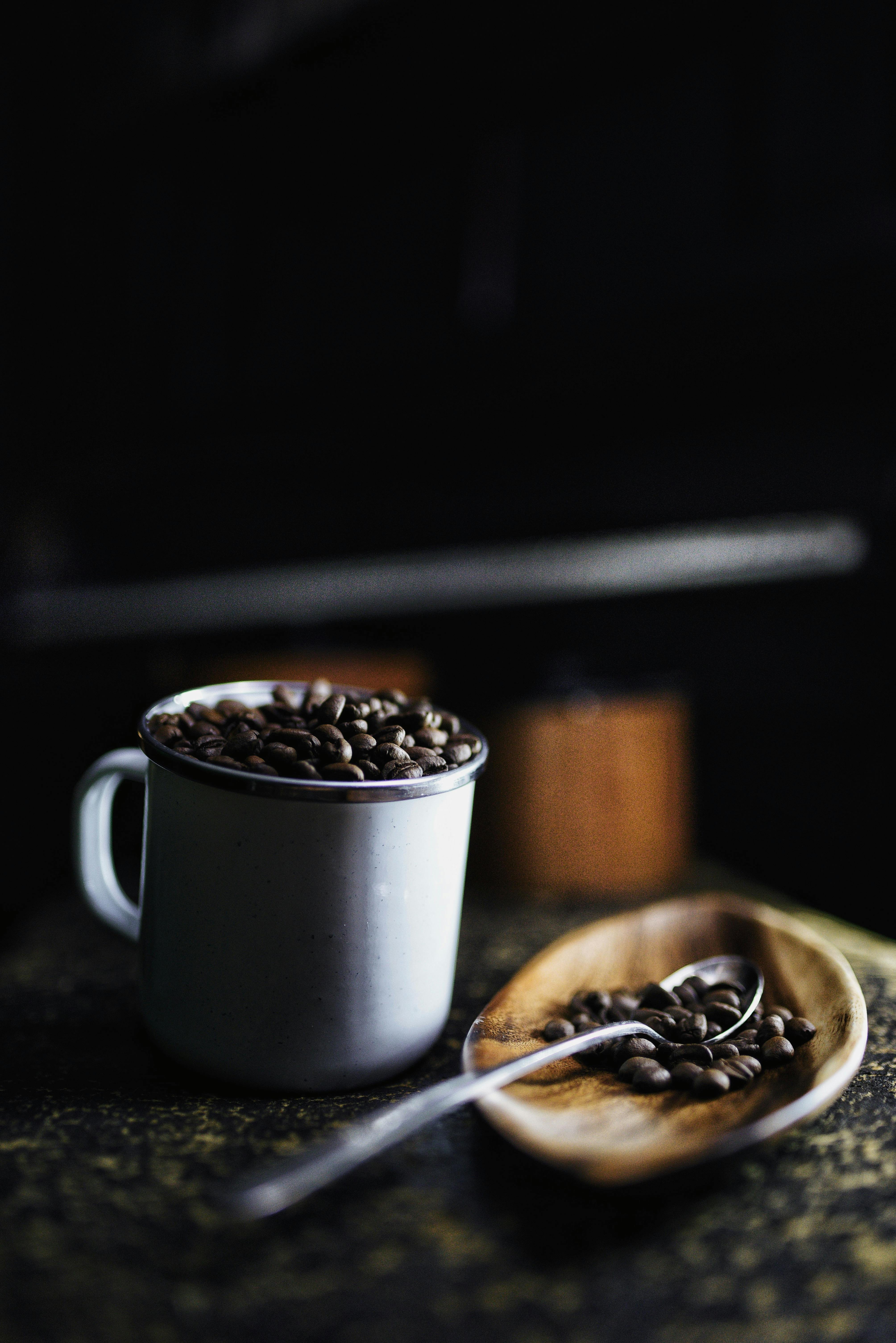 Rustic ceramic cup filled with coffee beans and spoon on wooden tray, perfect for coffee lovers.