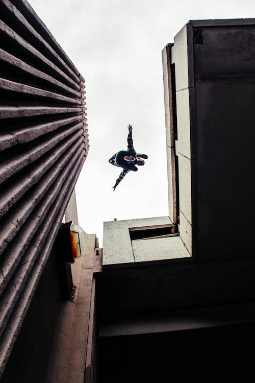 Free Man in Black Jacket and Blue Denim Jeans Jumping on Gray Concrete Building Stock Photo