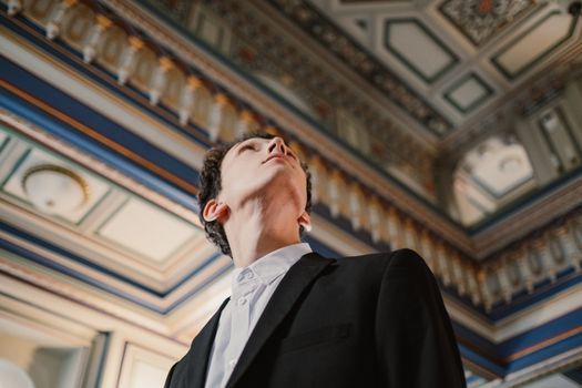 一位衣冠楚楚的男子仰望着华丽的室内天花板，上面展示着经典的建筑细节