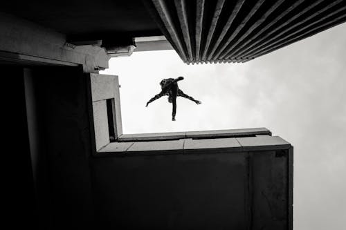 A Grayscale of a Person Jumping on Rooftops of Buildings