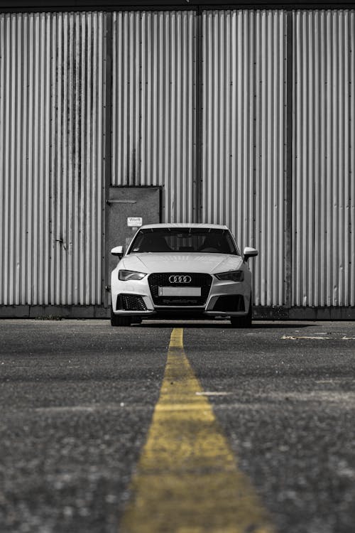 Ground level of modern white automobile parked on asphalt roadway with yellow marking line near metal wall with door on street in city