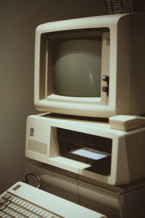 Retro obsolete white personal computer with small monitor and system unit with keyboard placed in room near gray wall