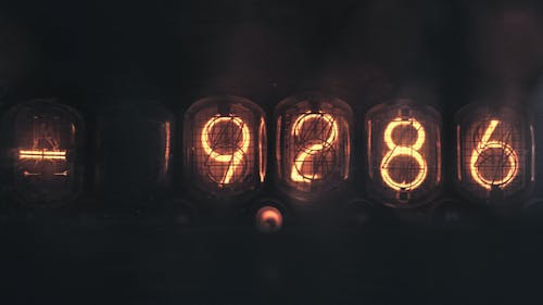 Electronic numerical counting machine with yellow illuminated number sequence using old fashioned tubes placed on black background in dark room