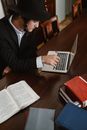 Man in Black Suit Jacket Using Macbook Air on Brown Wooden Table