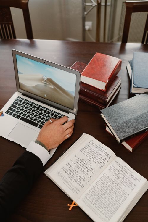 Free A person in formal wear works at a desk with a laptop and stacks of books, showcasing a study or work environment. Stock Photo