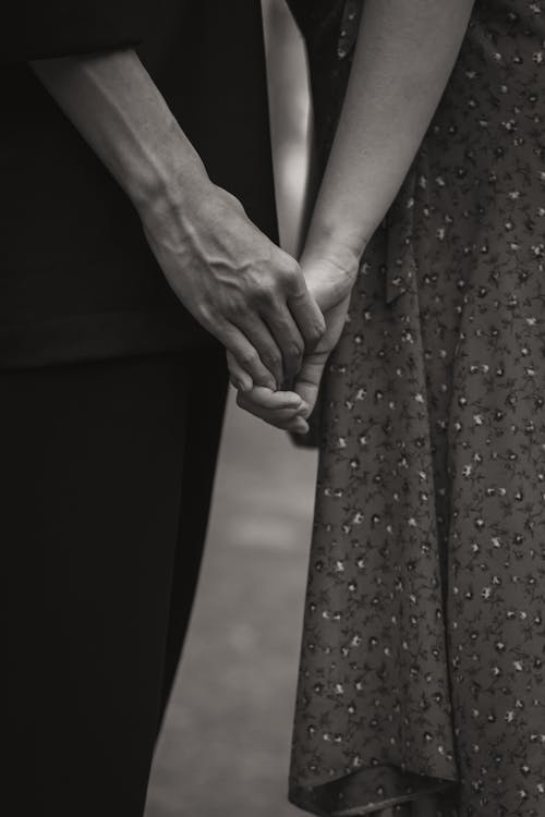 Free Black and white of unrecognizable romantic couple holding hands while standing in park with blurred background in nature on summer day Stock Photo