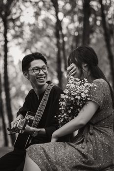 一对亚洲夫妇在森林中欢快地弹着吉他，分享浪漫时刻