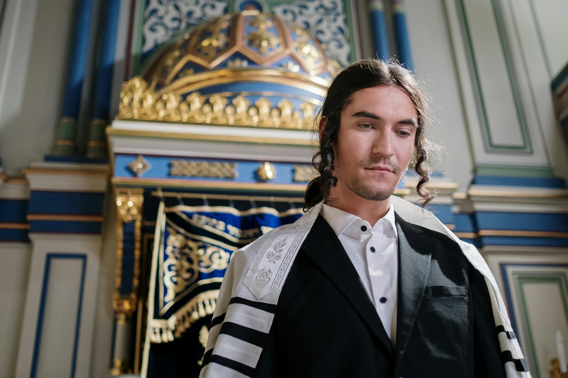 Young Man with Sidelocks Wearing Traditional Attire in front of Torah Ark in Synagogue