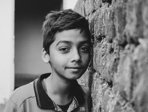 Free Black and white portrait of a young boy leaning against a brick wall with a thoughtful expression. Stock Photo