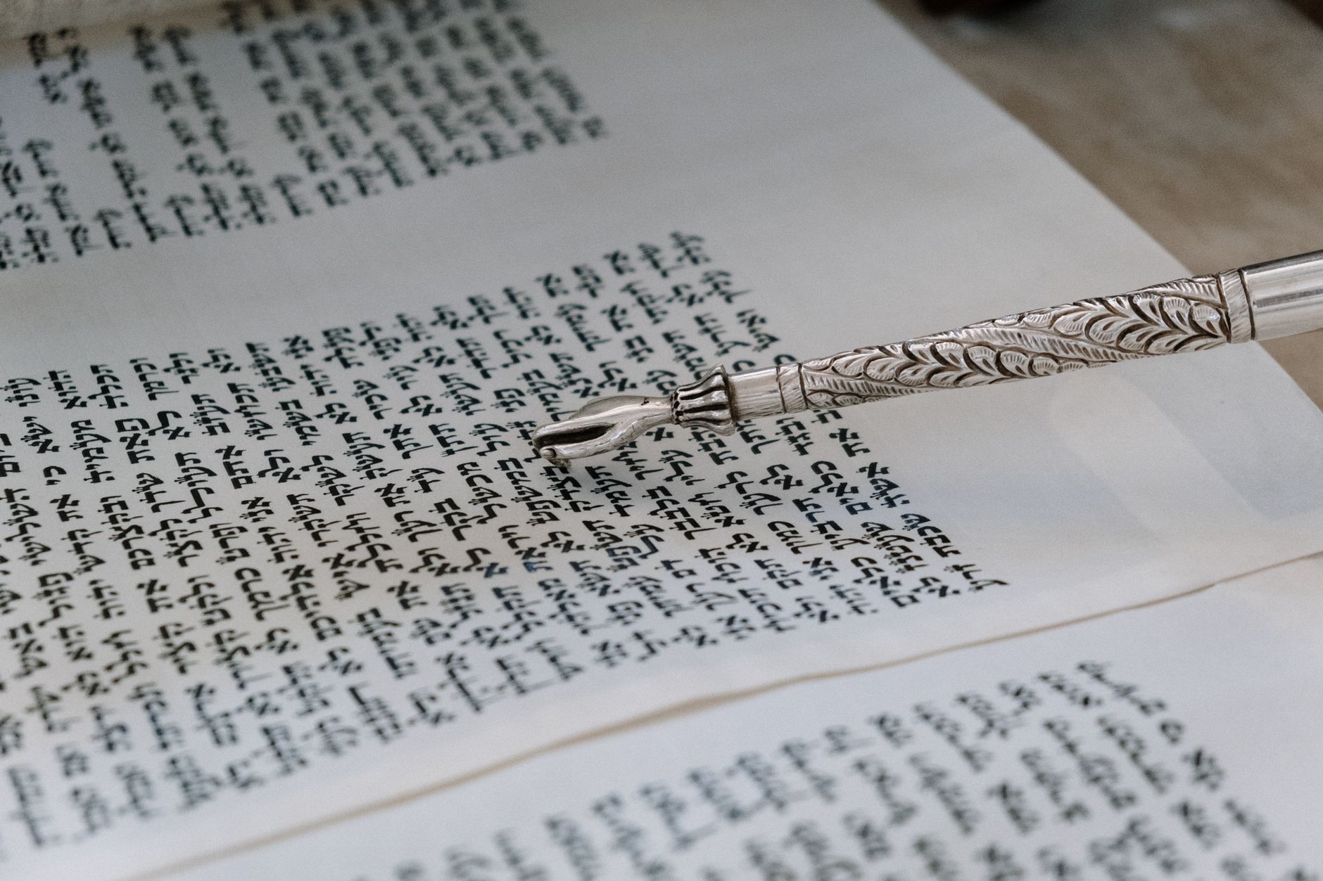 A detailed view of a silver yad pointing to Hebrew text in a Torah scroll.