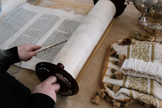 Person reading a Torah scroll using a yad in a traditional synagogue setting.