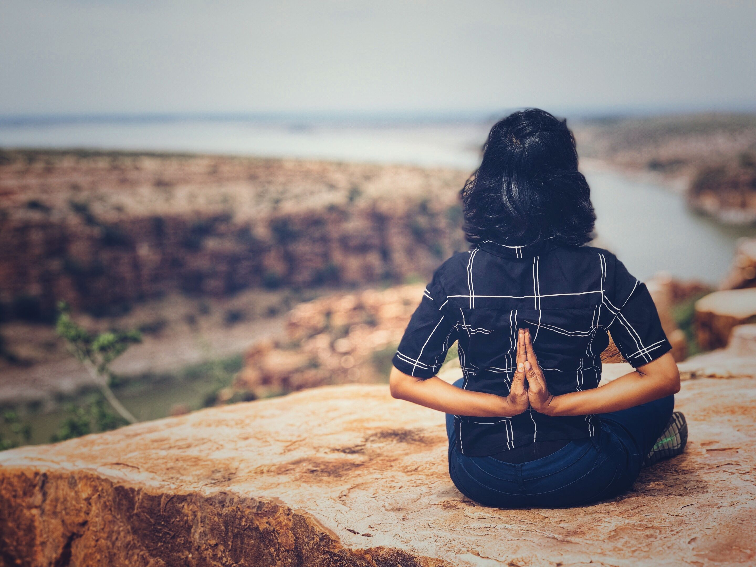 Woman practicing yoga on a cliff overlooking a canyon in India, promoting mindfulness and serenity.