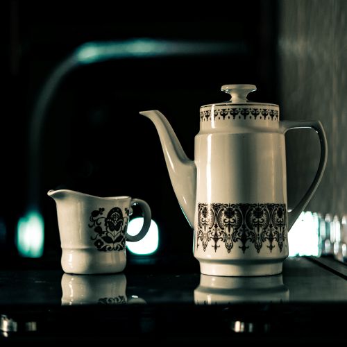 Free A detailed ceramic teapot and milk jug with intricate patterns, set against a dimly lit background. Stock Photo