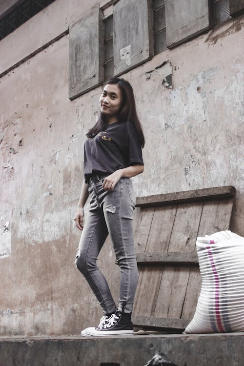 Free Woman Wearing Ripped Jeans Posing Beside a Wall Stock Photo