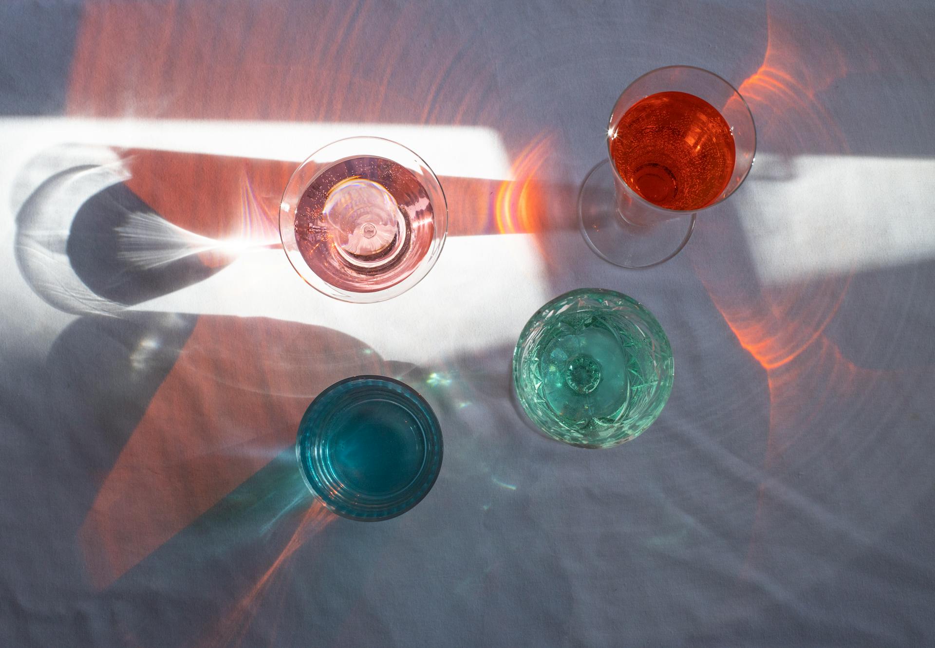 Top view of transparent glasses filled with different beverages and placed at sun beam