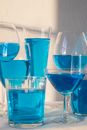 Composition of different crystal glasses filled with light blue beverage placed on table