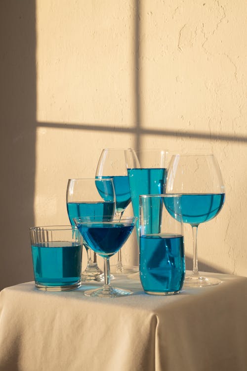 Arrangement of transparent glasses filled with blue drink and placed on table with white tablecloth