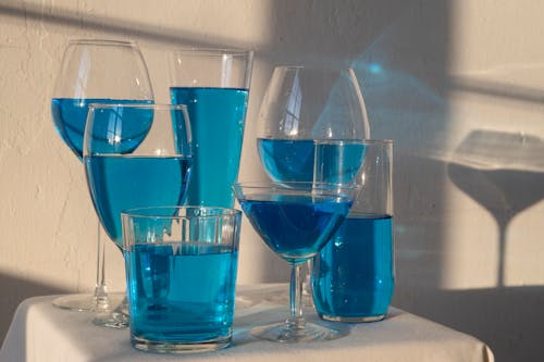 Transparent glasses filled with blue alcoholic drink standing on white tablecloth in sunlight