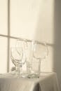 Composition of empty crystal glasses placed on table with white tablecloth in sunlight