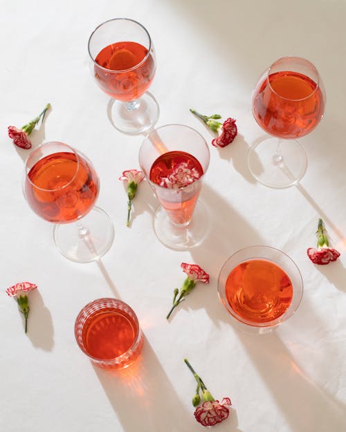 From above of composition of pink flowers and transparent glasses filled with red drink