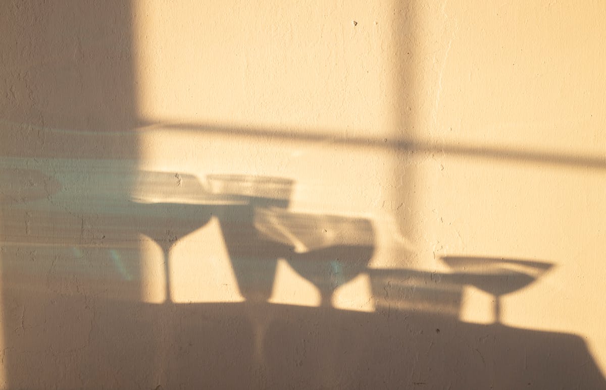 Shadows of different crystal glasses filled with drinks reflecting on white wall in sunlight