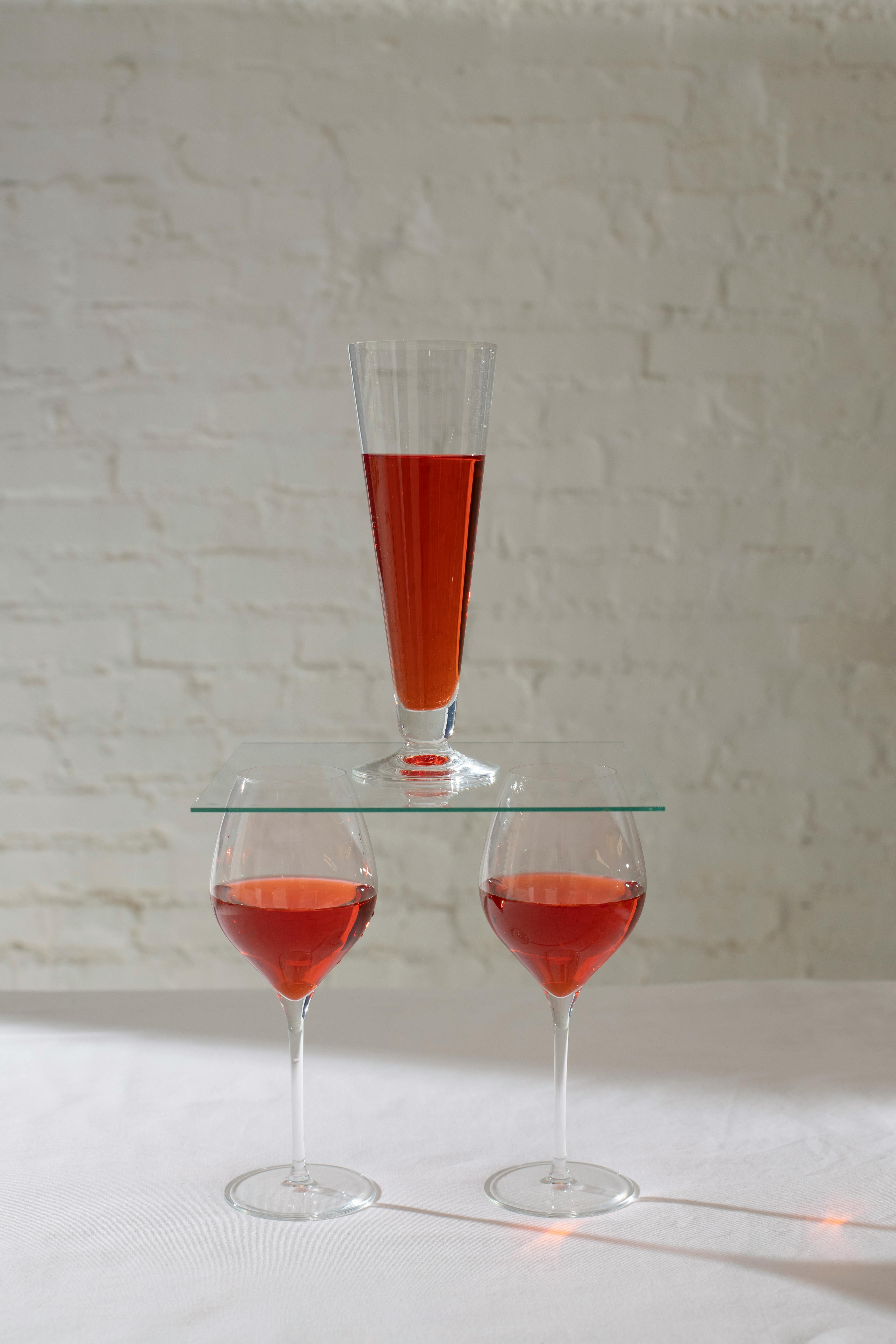 在明亮的房间里，靠近砖墙的白桌子上，放着一杯装有红色酒精饮料的酒杯