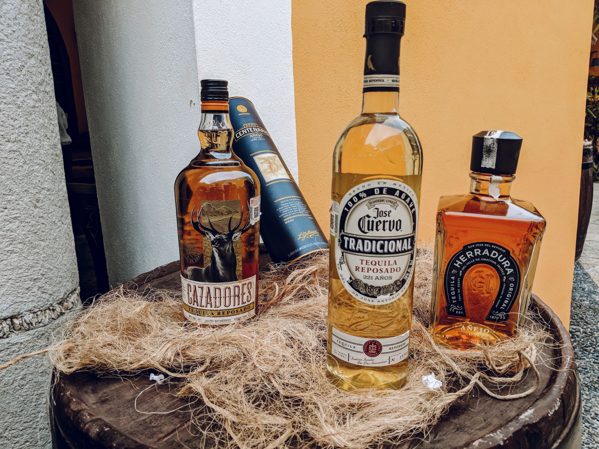 A collection of tequila bottles arranged outdoors on a rustic barrel.